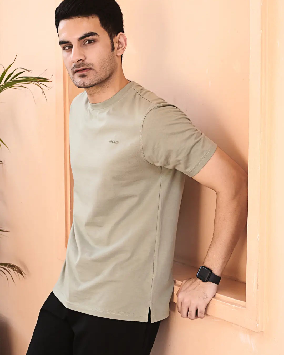 Man wearing a light gray crew neck cotton t-shirt, standing against a beige wall.