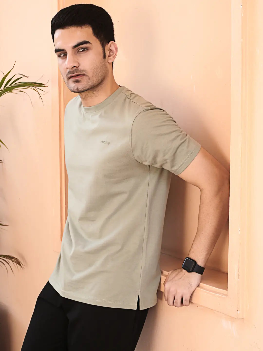Man wearing a light gray crew neck cotton t-shirt, standing against a beige wall.