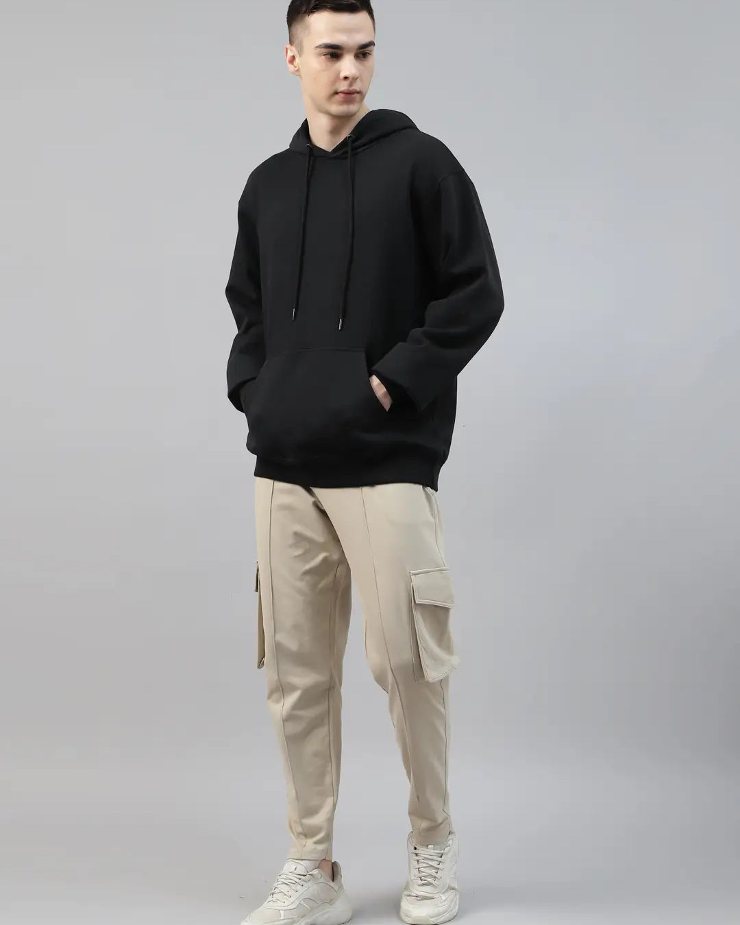 Person wearing a black hoodie and beige cargo pants on a gray background