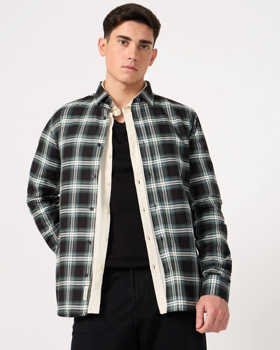 Man wearing a black and green plaid shirt over a black t-shirt on a white background