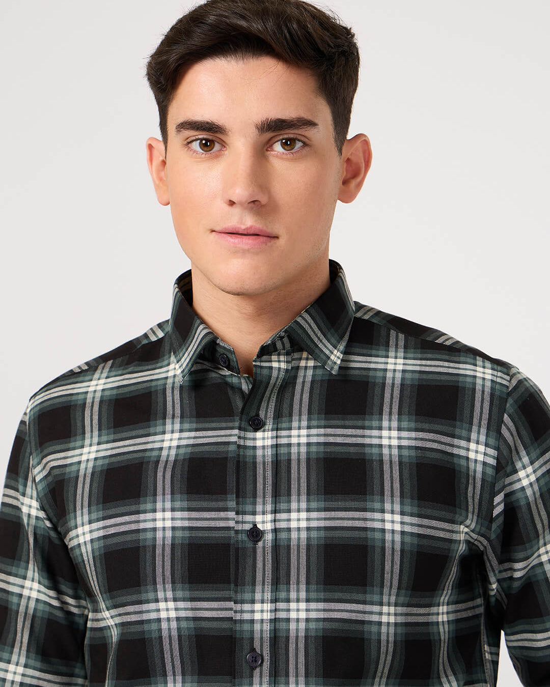 Man wearing a black and green plaid shirt made with pure cotton against a plain background