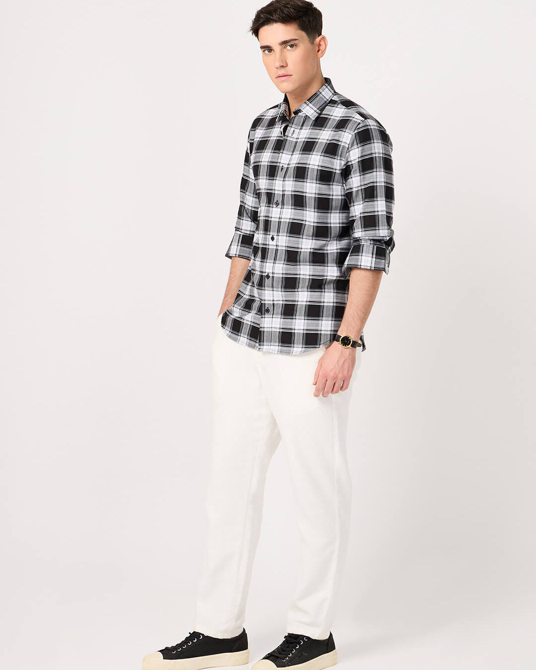 Man wearing a black and white checkered shirt with white pants on a white background