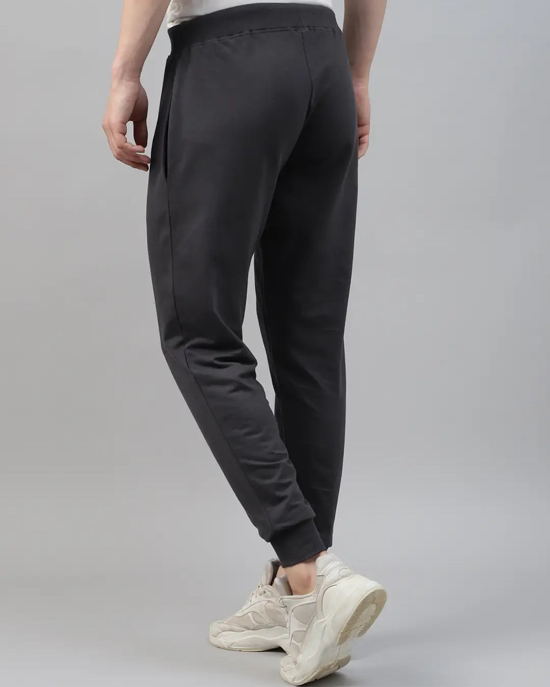 Person wearing dark grey jogger pants and white sneakers on a gray background