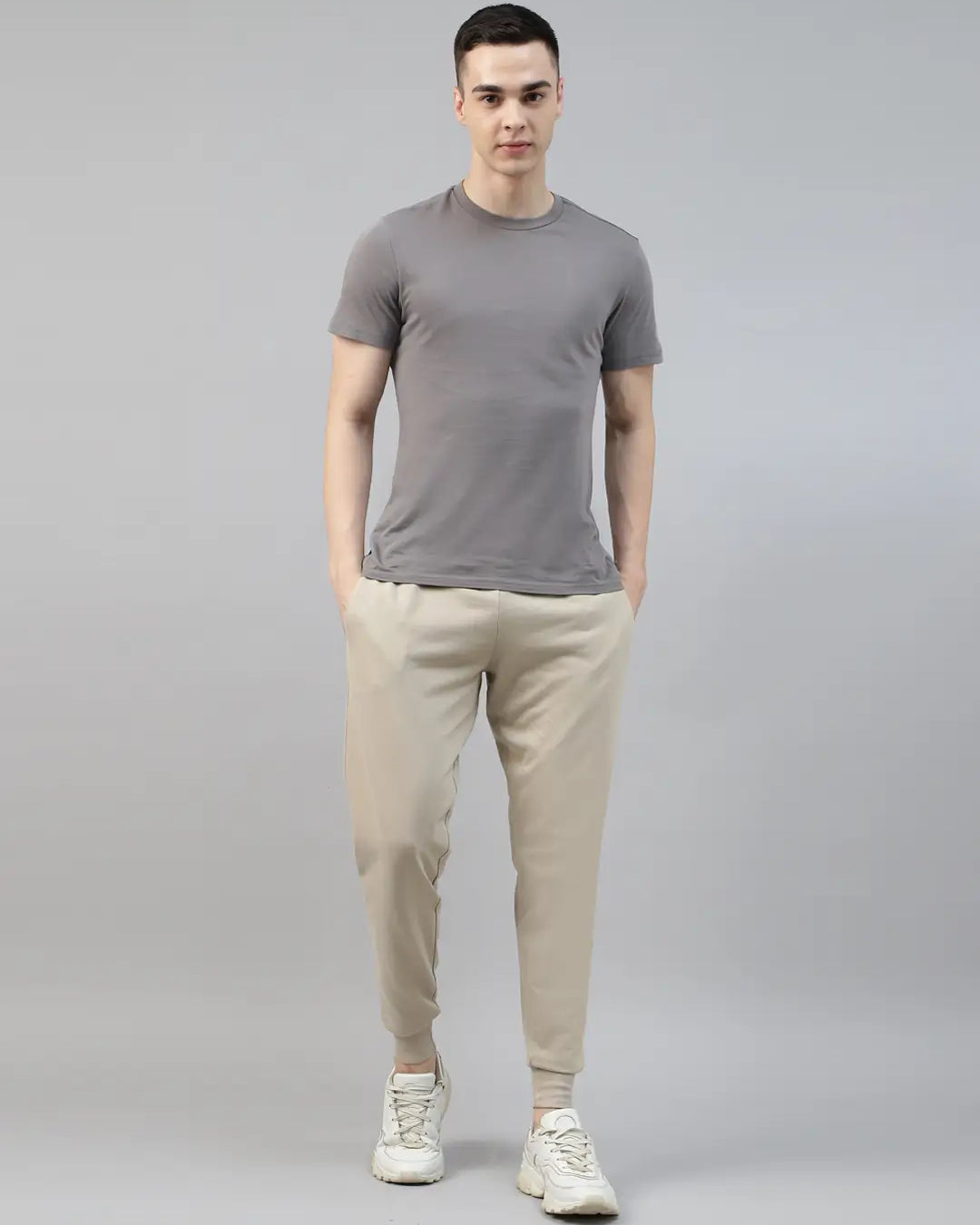 Man wearing a gray t-shirt and beige jogger pants on a gray background