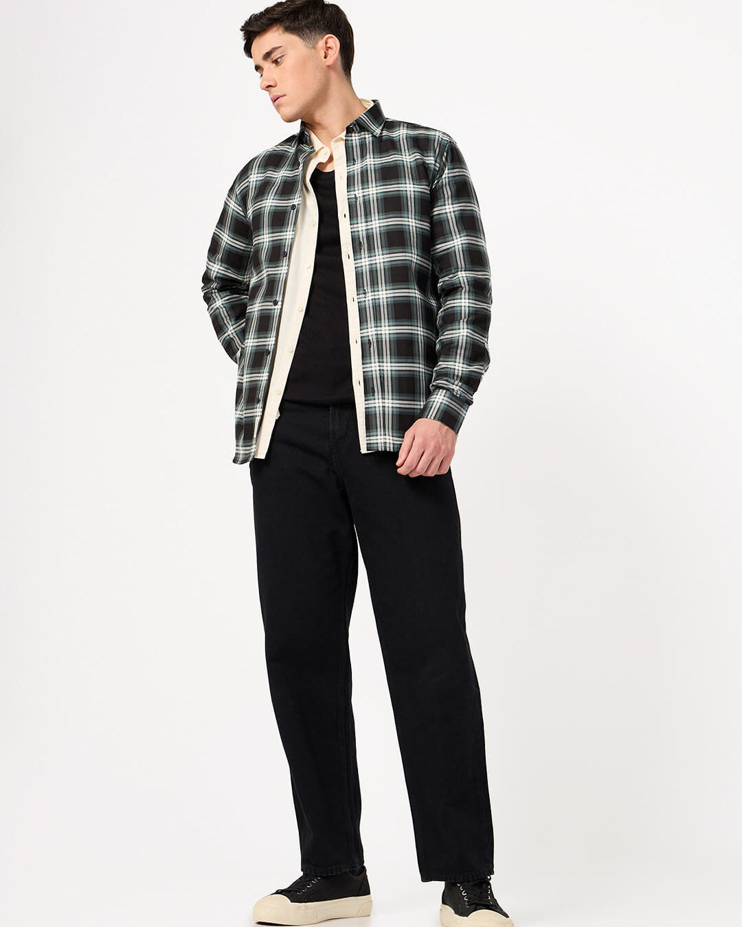 Man wearing a black and green plaid shirt over a black t-shirt with black pants on a white background
