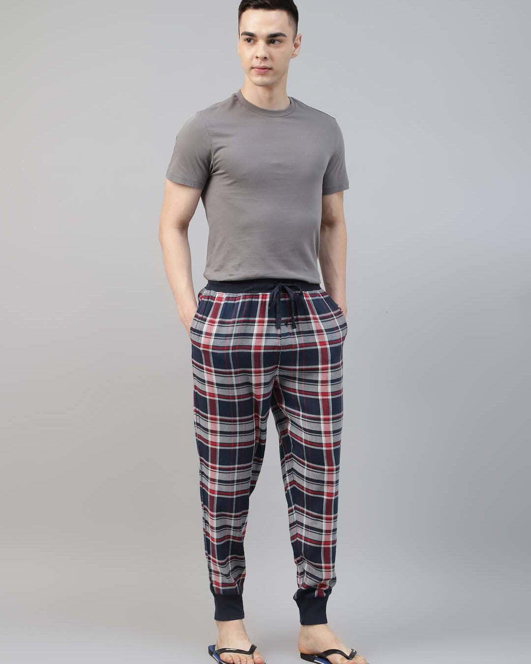 Man wearing a gray t-shirt and plaid jogger pant on a gray background