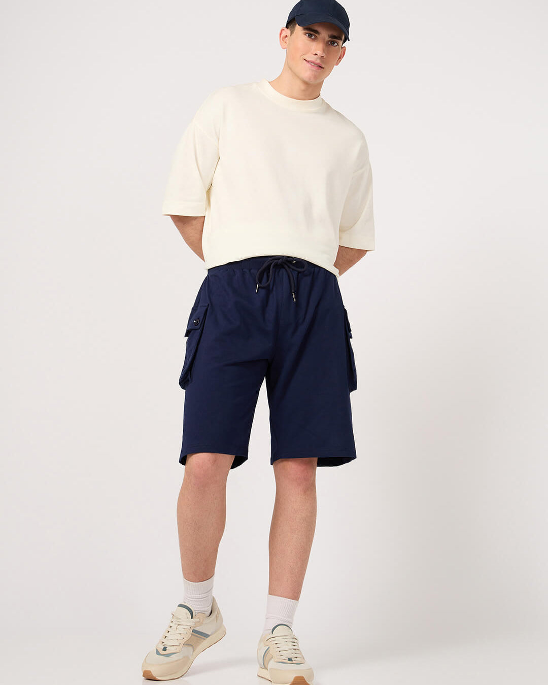 Person wearing a white shirt, navy shorts, and a cap on a white background