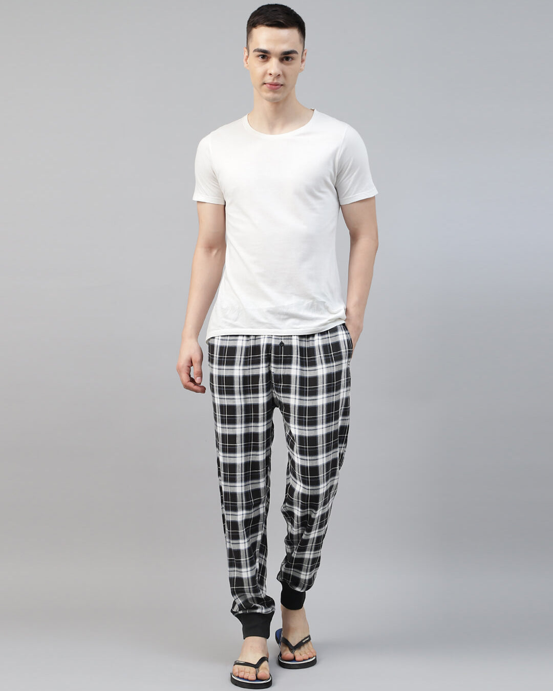 Man wearing a white t-shirt and black and white checkered pants on a gray background