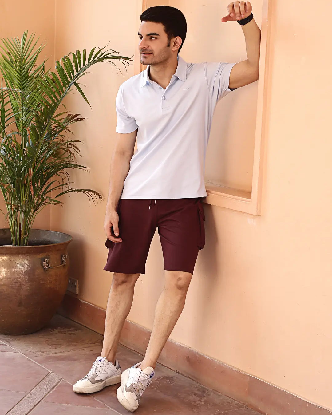 Man in a light sky blue polo t shirt and maroon shorts standing against a wall