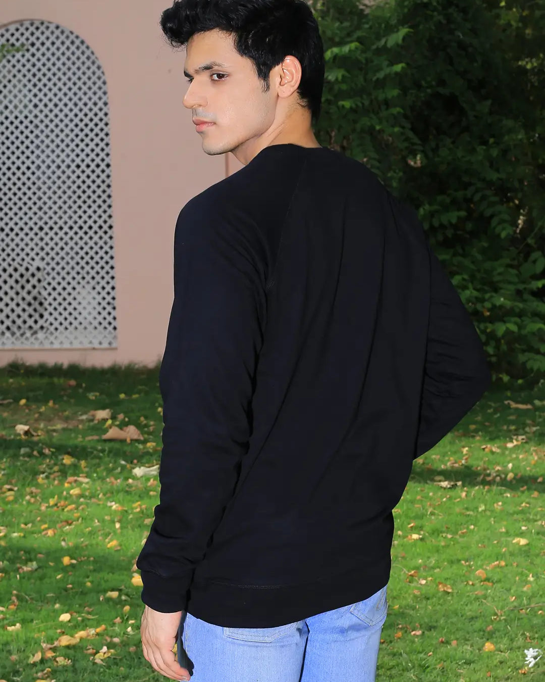 Man wearing a black sweatshirt and light blue jeans standing outdoors