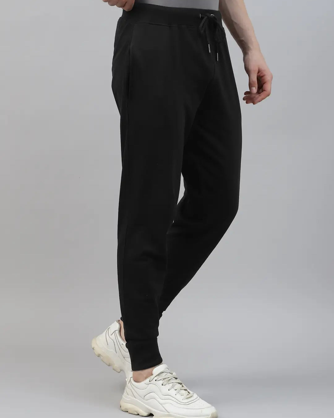 Person wearing black jogger pants and white sneakers on a gray background