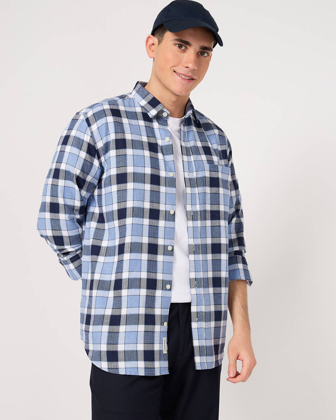 Man wearing a blue and white checkered shirt with a navy cap on a light gray background