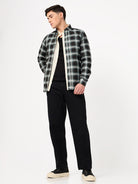 Man wearing a black and green plaid shirt over a black t-shirt with black pants on a white background